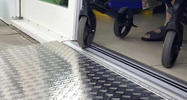 Dieses Bild zeigt eine Fenstertür mit Holzprofilen, die trotz eines ca. 7 cm hohen Türschwellen-Rückbaus erhalten werden konnte. „Das erfordert eine millimetergenaue Arbeit, doch die Dankbarkeit und Freude meiner Kunden über die Befreiung von hinderlichen und gefährlichen Türschwellen ist mir dies Wert“, berichtet Bernhard Strauß, Geschäftsführer der Glaserei Strauß aus Freiburg. „Neben der längst möglichen Magnet-Nullschwelle für den Neubau ist hier eine Lösung für den Bestand zu sehen, die direkt auf den Estrich aufgesetzt werden kann. Durch diese Möglichkeit wird jede Türanschlagdichtung selbst im Bestand überflüssig.“