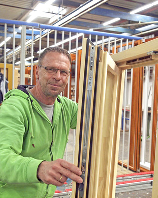 Joachim Kleinert präsentiert ein fertig zusammengesetztes Holzfenster mit Fensterfalzlüftern von Regel-air.