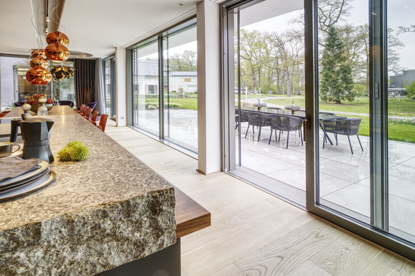 Küche und Essbereich verschmelzen in der Villa zu einem einzigen großen Raum. Der dank der Hebe-Schiebe-­Elemente nahtlose Übergang nach draußen schafft eine einladende Atmosphäre.