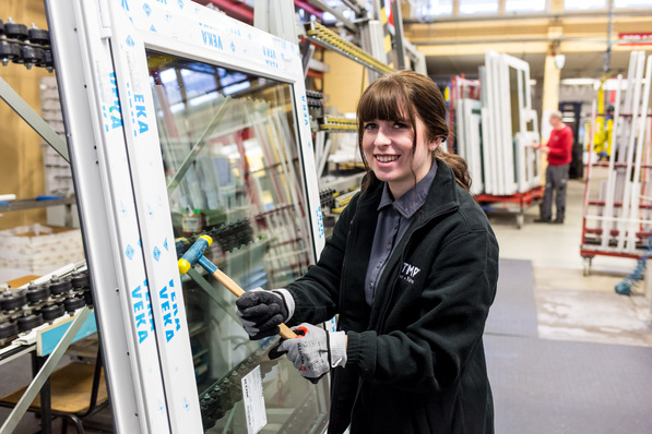 Jobbloggerin Franzi bei der "Hochzeit" (wenn Blendrahmen und Flügel und die Isolierglaseinheit zu einem Fenster zusammengebaut werden): Mit einem speziellen Hammer werden Glasleisten an einem Fenster angebracht.
