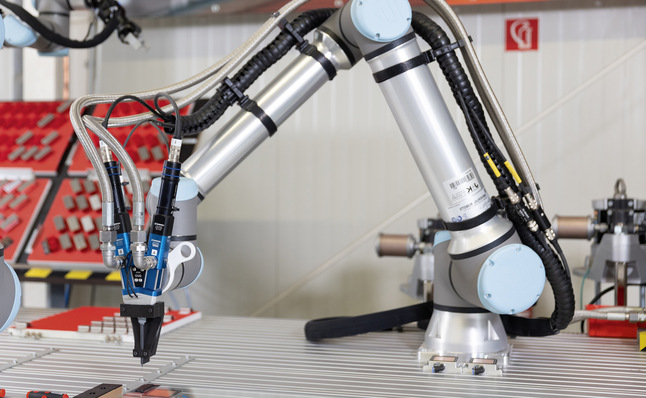 Cobots können ohne Umhausung vielfältig eingesetzt werden: Hier klebt ein Cobots Befestigungs­elemente auf Glasscheiben.