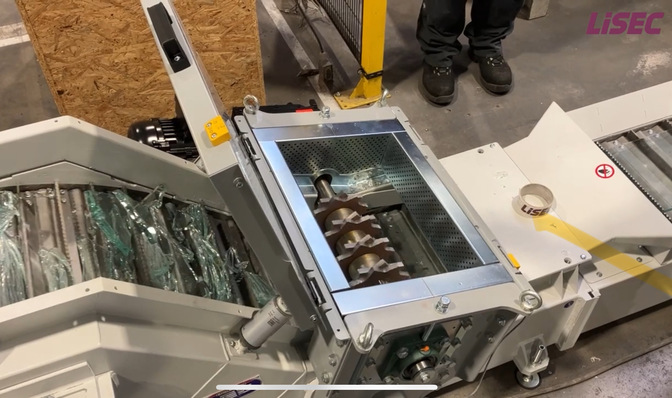 „Produktionshalle in der Glasverarbeitung mit Maschinen zur Bearbeitung von Glasstücken und Metallkomponenten; ein Mitarbeiter bedient die Anlage auf einem Betonboden. - © Lisec