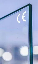 „Nahaufnahme einer Glasscheibe mit CE-Kennzeichnung, die für geprüfte Qualitäts- und Sicherheitsstandards in der Fenstertechnik steht, vor einem unscharfen Hintergrund innerhalb eines technisch-gewerblichen Umfelds. - © Fineo