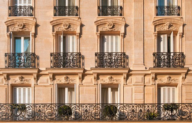Straßenansicht einer alten, eleganten Wohnhausfassade in Paris mit Fenstertüren und ­Absturzsicherungen in Form von Geländern.