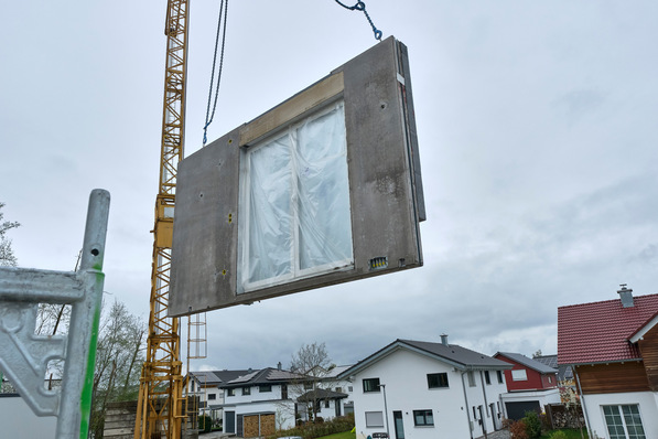 Per Kran werden die hoch vorgefertigten Betonwände auf der Baustelle montiert. Fenster, Dämmung und technische Vorinstallationen sind bereits integriert.